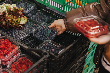 Close-up of transparent plastic containers with fresh berries in female hands of buyer. Packages...