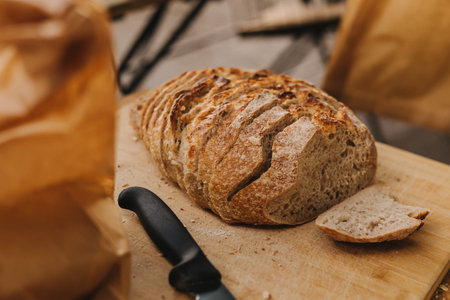 Close-up of chef's hands cutting whole grain bread with a knife on a wooden table. Concept of healthy eating and traditional bakery. Selective focusの写真素材