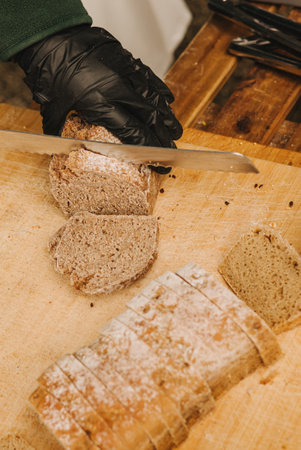 Close-up of chef's hands cutting whole grain bread with a knife on a wooden table. Concept of healthy eating and traditional bakery. Selective focusの写真素材