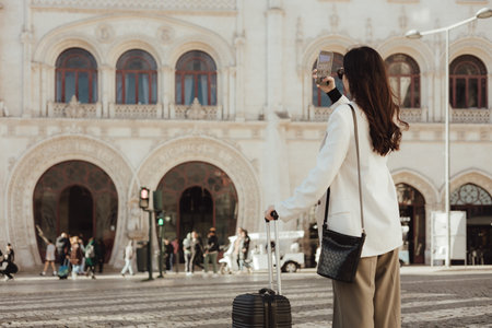 Vlogger traveler woman with suitcase using phone at train station in Lisbon. Business travel and solo tourism concept. Part of seriesの写真素材