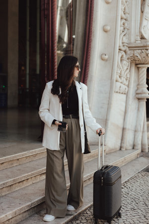 Vlogger traveler woman with suitcase using phone at train station in Lisbon. Business travel and solo tourism concept. Gen Z girl influencer shooting social media stories on the street.の写真素材