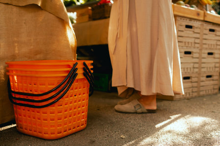 Top view of plastic orange shopping basket and feet of a buyer at local urban market. Organic produce on sale at outdoor farmer market. European urban setting. Close up. Part of the series.の写真素材
