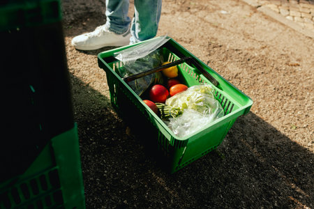 Front view of plastic shopping basket with fresh vegetables and feet of a buyer at local urban market. Organic produce on sale at outdoor farmer market. Part of the series.の写真素材