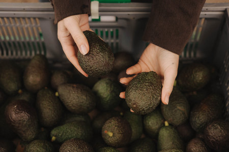 Close up of woman buying green avocado on the local Farmers market. Mature Female Customer Shopping At Farmers Market Stall. Close up. Part of the series.の写真素材