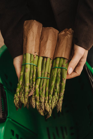 Close up of woman buying green asparagus on the local Farmers market. Mature Female Customer Shopping At Farmers Market Stall. Close up. Part of the series.の写真素材