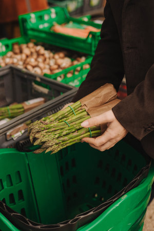 Close up of woman buying green asparagus on the local Farmers market. Mature Female Customer Shopping At Farmers Market Stall. Close up. Part of the series.の写真素材