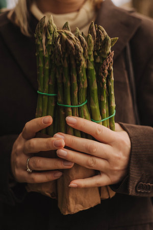 Close up of woman buying green asparagus on the local Farmers market. Mature Female Customer Shopping At Farmers Market Stall. Close up. Part of the series.の写真素材
