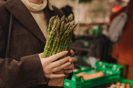 Close up of woman buying green asparagus on the local Farmers market. Mature Female Customer Shopping At Farmers Market Stall. Close up. Part of the series.の写真素材