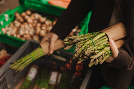 Close up of woman buying green asparagus on the local Farmers market. Mature Female Customer Shopping At Farmers Market Stall. Close up. Part of the series.の写真素材