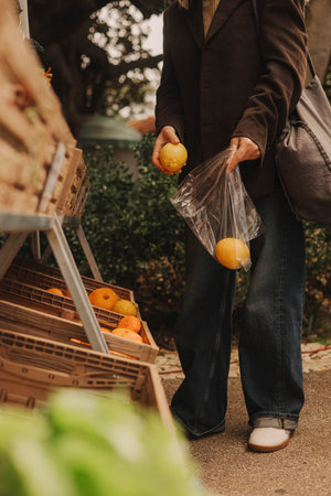 Close-up of female hands putting lemons into a bag at a local market. Organic produce on sale at outdoor farmer market. Selling fresh crops and veggies harvest. Close up. Part of the seriesの写真素材