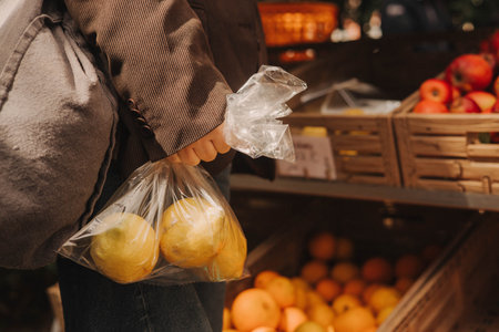 Close-up of female hands putting lemons into a bag at a local market. Organic produce on sale at outdoor farmer market. Selling fresh crops and veggies harvest. Close up. Part of the seriesの写真素材