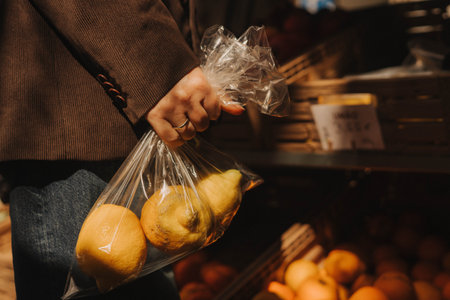 Close-up of female hands putting lemons into a bag at a local market. Organic produce on sale at outdoor farmer market. Selling fresh crops and veggies harvest. Close up. Part of the seriesの写真素材