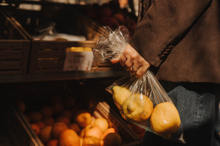 Close-up of female hands putting lemons into a bag at a local market. Organic produce on sale at outdoor farmer market. Selling fresh crops and veggies harvest. Close up. Part of the seriesの写真素材