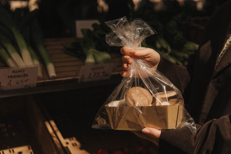 Close up of hand with a exotic mushrooms in polyethylene bag on the local Farmers market. Mature Female Customer Shopping At Farmers Market Stall. Woman buying vegetables. Close up. Part of the seriesの写真素材