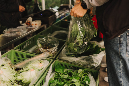 Close up of hand with a greens in polyethylene bag on the local Farmers market. Mature Female Customer Shopping At Farmers Market Stall. Woman buying vegetables. Close up. Part of the seriesの写真素材