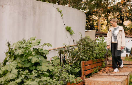 Portrait of a middle-aged woman as florist taking care of flowers and plants in garden with vintage greenhouse eco-farm. Concept green tourism, slow life, gardening, eco friendly. Part of the seriesの写真素材
