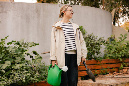 Portrait of a middle-aged woman as florist taking care of flowers and plants in garden with vintage greenhouse eco-farm. Concept green tourism, slow life, gardening, eco friendly. Part of the seriesの写真素材