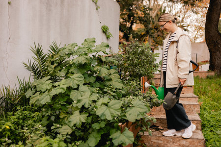 Portrait of a middle-aged woman as florist taking care of flowers and plants in garden with vintage greenhouse eco-farm. Concept green tourism, slow life, gardening, eco friendly.の写真素材