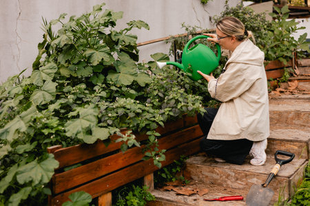 Portrait of a middle-aged woman as florist taking care of flowers and plants in garden with vintage greenhouse eco-farm. Concept green tourism, slow life, gardening, eco friendly. Part of the seriesの写真素材