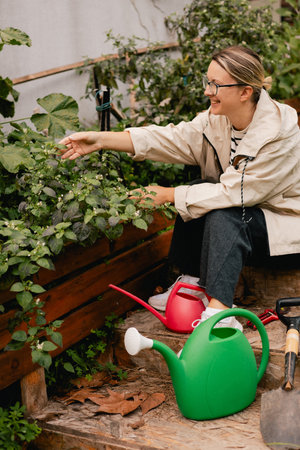Portrait of a middle-aged woman as florist taking care of flowers and plants in garden with vintage greenhouse eco-farm. Concept green tourism, slow life, gardening, eco friendly. Part of the seriesの写真素材
