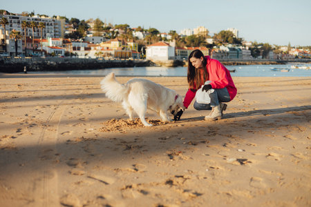 A female ecologist volunteer with dog cleans the beach on the seashore from plastic and other waste. Garbage recycle and environmental care concept.の写真素材