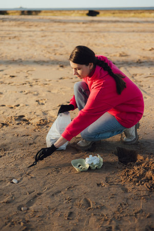 A female ecologist volunteer cleans the beach on the seashore from plastic and other waste. Garbage recycle and environmental care concept. Part of a seriesの写真素材