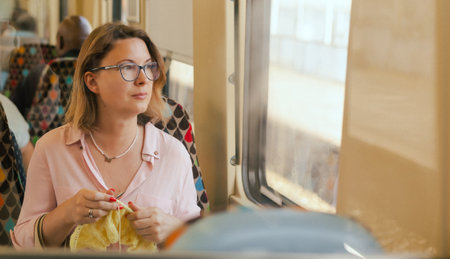 Attractive woman on public transport in knitting work activity using wool. Relaxed woman enjoying...