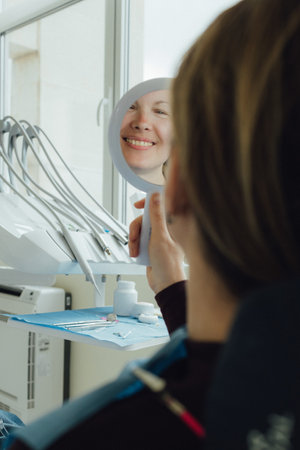 Smiling mature woman in a dental chair with mirror. Appointment at clinic. Tooth whitening, cleaning...