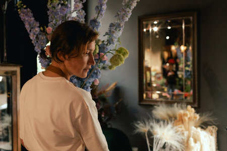 Middle-aged female florist in apron arranging fresh flowers for bouquet in the flower shop. Small local business. Part of a series. Soft focusの写真素材