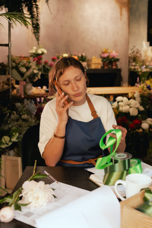 Middle-aged female florist in apron arranging flowers. She is arranging logistics, and delivery, taking orders. Small local business. Part of a series. Soft focusの写真素材