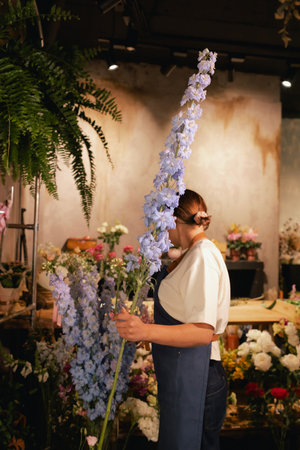 Middle-aged female florist in apron arranging fresh flowers for bouquet in the flower shop. Small local business. Part of a series. Soft focusの写真素材