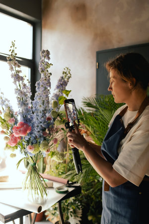 Small flower shop. A woman writes a video blog or online course. Flower school concept. Florist woman creates flower arrangement. . Local business. Part of a series.の写真素材