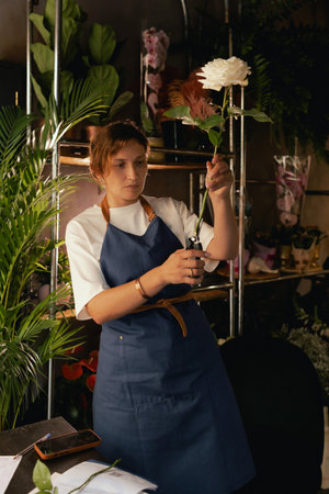 Middle-aged female florist in apron arranging fresh flowers for bouquet in the flower shop. Small local business. Part of a series. Soft focusの写真素材