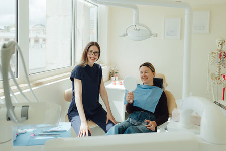 Smiling mature woman at dental check-up with young female dentist. Appointment at clinic. Tooth whitening, cleaning or oral, mouth and gum care at hospital. Soft focus. Part of a series. Close-up.の写真素材