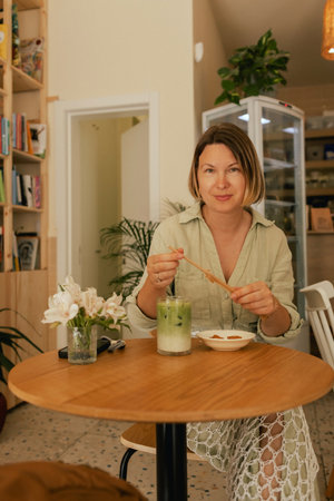 Middle-aged woman scrolls her social media feed on mobile phone in a cozy cafe. Small business....