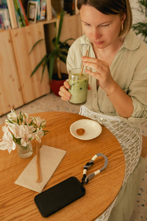 Middle-aged woman scrolls her social media feed on mobile phone in a cozy cafe. Small business. Using phone for business, online shopping, transfer money, financial, internet banking. Part of a seriesの写真素材