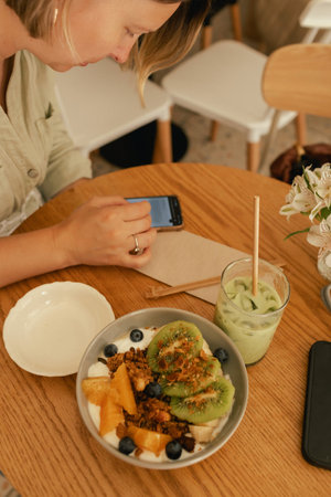Middle-aged woman scrolls her social media feed on mobile phone in a cozy cafe. Small business. Using phone for business, online shopping, transfer money, financial, internet banking. Part of a seriesの写真素材