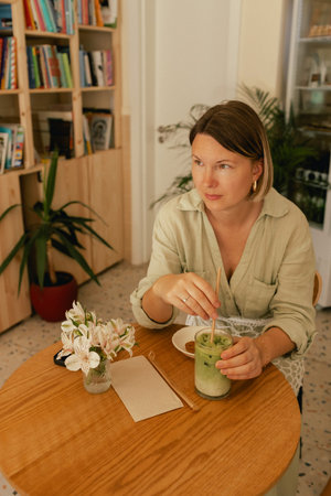 Middle-aged woman scrolls her social media feed on mobile phone in a cozy cafe. Small business. Using phone for business, online shopping, transfer money, financial, internet banking. Part of a seriesの写真素材