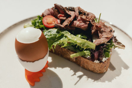 Sandwich with meat, egg and with freshly greens. Crop delicious breakfast served on wooden table in sunny cafe. Part of a series.の写真素材