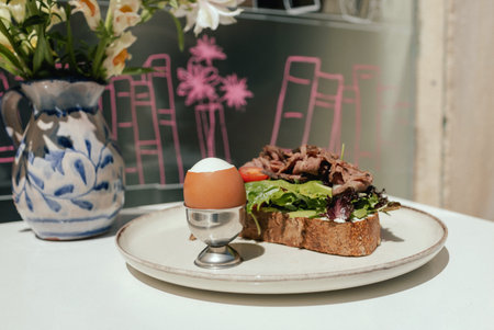 Sandwich with meat, egg and with freshly greens. Crop delicious breakfast served on wooden table in sunny outdoor cafe. Part of a series.の写真素材