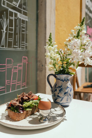Sandwich with meat, egg and with freshly greens. Crop delicious breakfast served on wooden table in sunny outdoor cafe. Part of a series.の写真素材