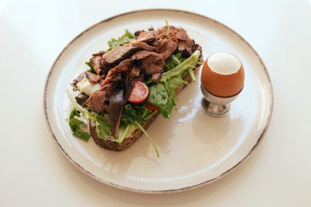 Sandwich with meat, egg and with freshly greens. Crop delicious breakfast served on wooden table in sunny cafe. Part of a series.の写真素材