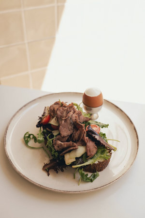 Sandwich with meat, egg and with freshly greens. Crop delicious breakfast served on wooden table in sunny cafe. Part of a series.の写真素材
