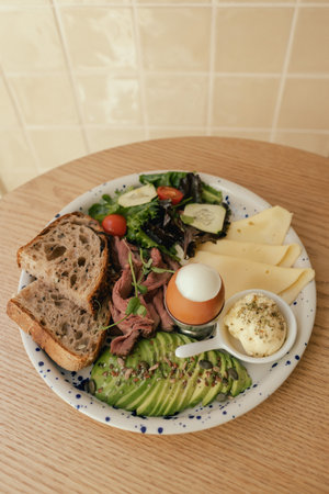 Sandwich with meat, avocado, egg and with freshly greens. Crop delicious breakfast served on wooden table in sunny indoor cafe. Part of a series.の写真素材