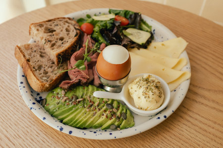 Sandwich with meat, avocado, egg and with freshly greens. Crop delicious breakfast served on wooden table in sunny indoor cafe. Part of a series.の写真素材
