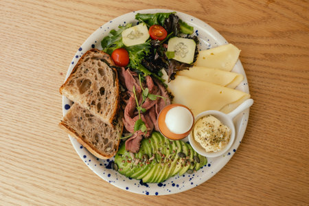 Sandwich with meat, avocado, egg and with freshly greens. Crop delicious breakfast served on wooden table in sunny indoor cafe. Part of a series.の写真素材