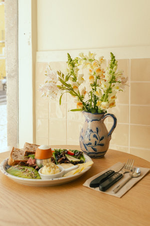 Sandwich with meat, avocado, egg and with freshly greens. Crop delicious breakfast served on wooden table in sunny indoor cafe. Part of a series.の写真素材
