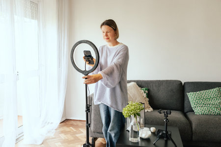 Middle-aged woman beauty blogger filming skincare product unboxing at home with ring light. User-generated content UGC for online store promotion. Vlogger live streaming. Part of a seriesの写真素材