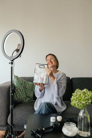 Middle-aged woman beauty blogger filming skincare product unboxing at home with ring light. User-generated content UGC for online store promotion. Vlogger live streaming. Part of a seriesの写真素材