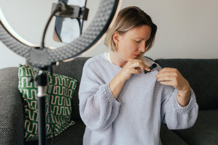 Middle-aged woman beauty blogger filming skincare product unboxing at home with ring light. User-generated content UGC for online store promotion. Vlogger live streaming. Part of a seriesの写真素材